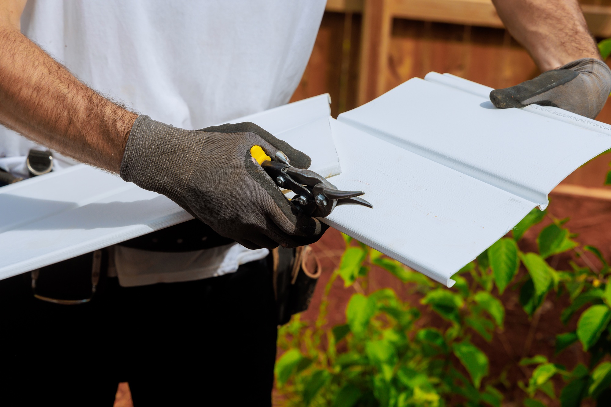 An individual cuts plastic vinyl siding to size before it is installed using a scissors