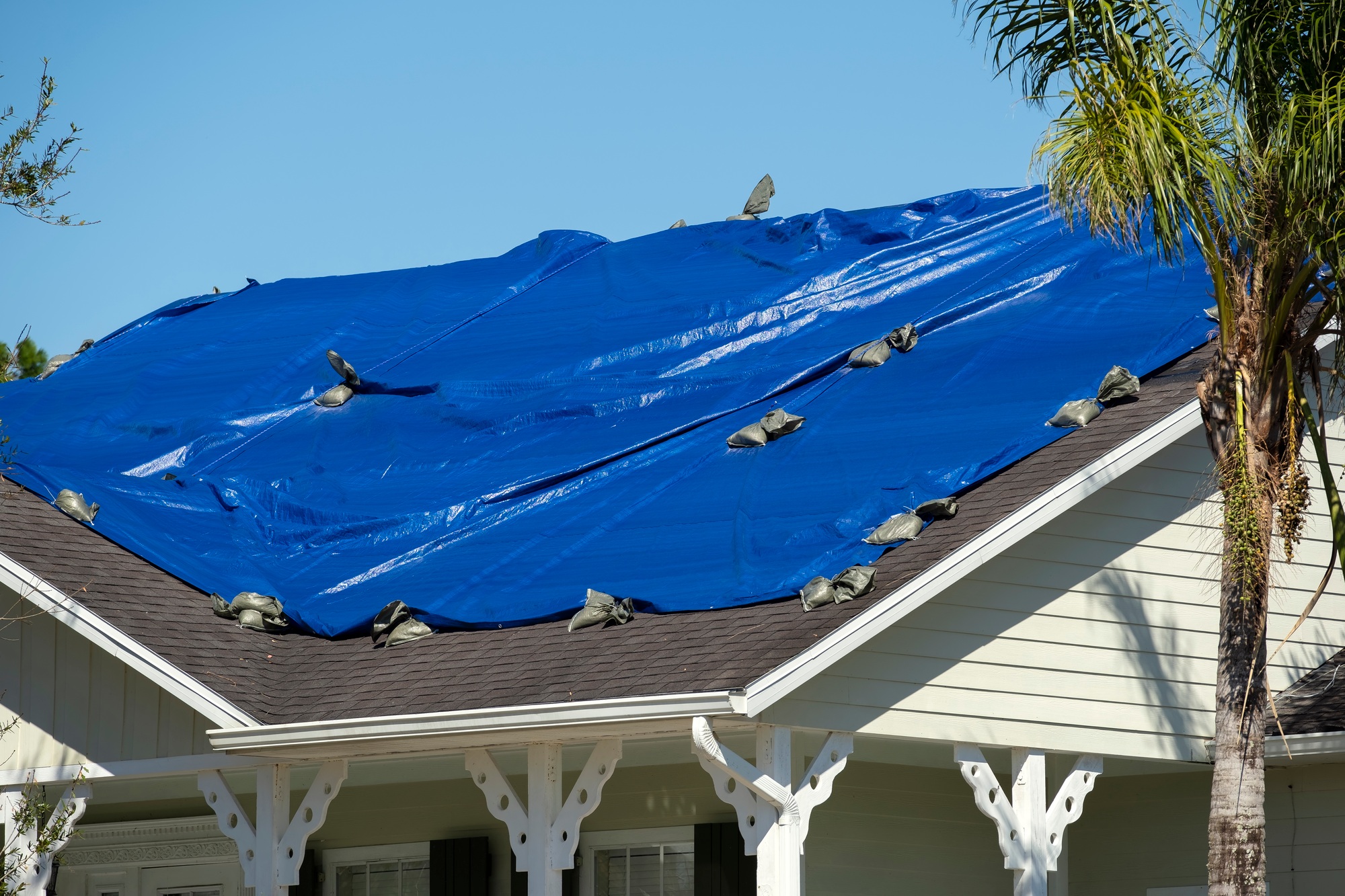 Damaged in hurricane Ian house roof covered with blue protective tarp against rain water