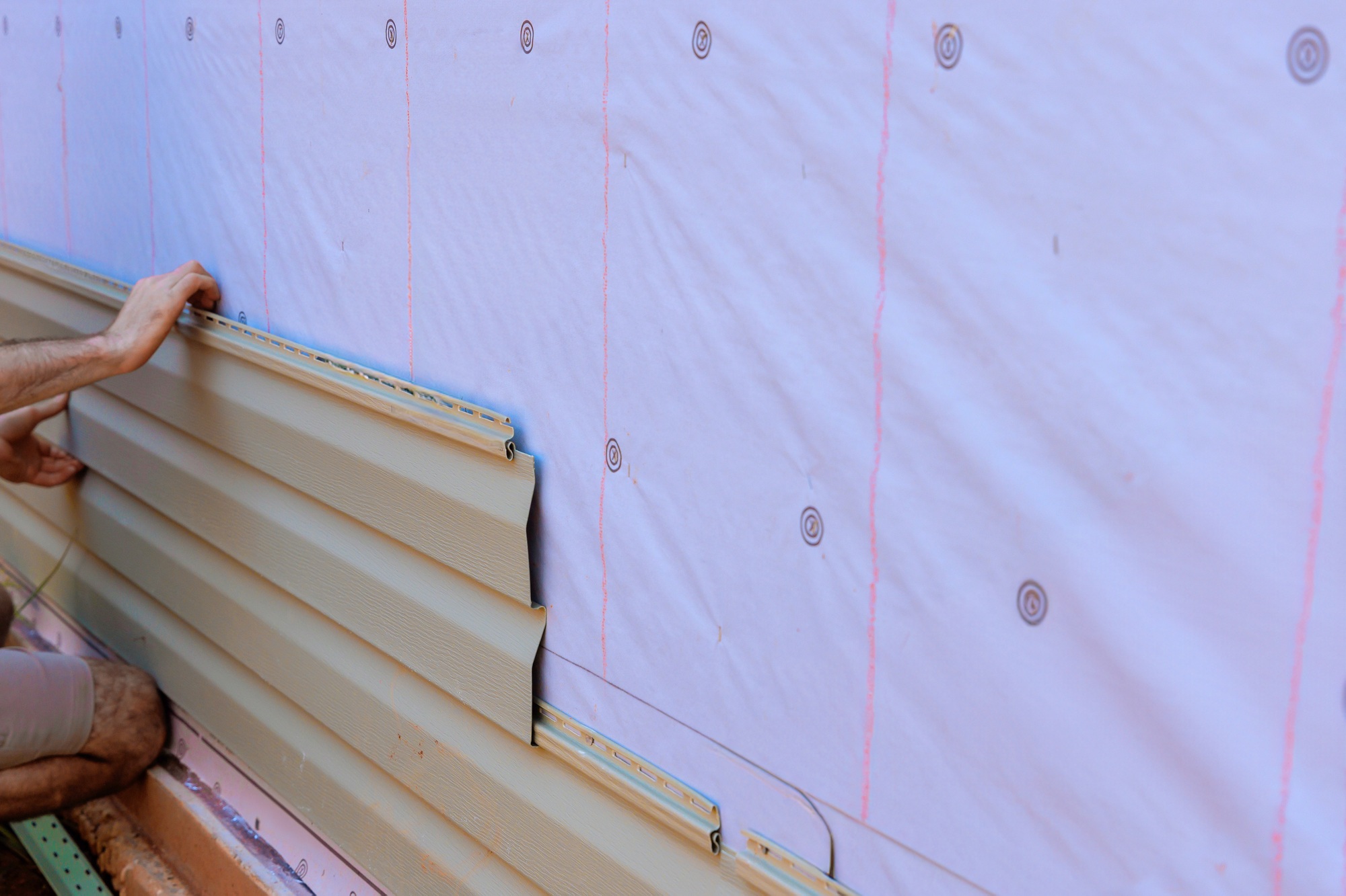 In process of installing vinyl siding on new home facade, a handyman installs vinyl PVC siding