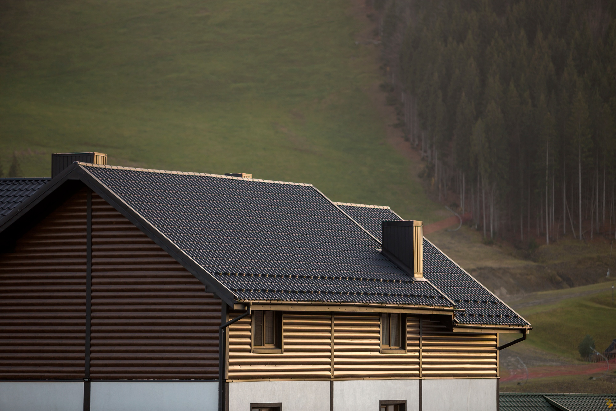 Roof of cottage with siding walls, brown shingle roof and high chimneys in ecological area