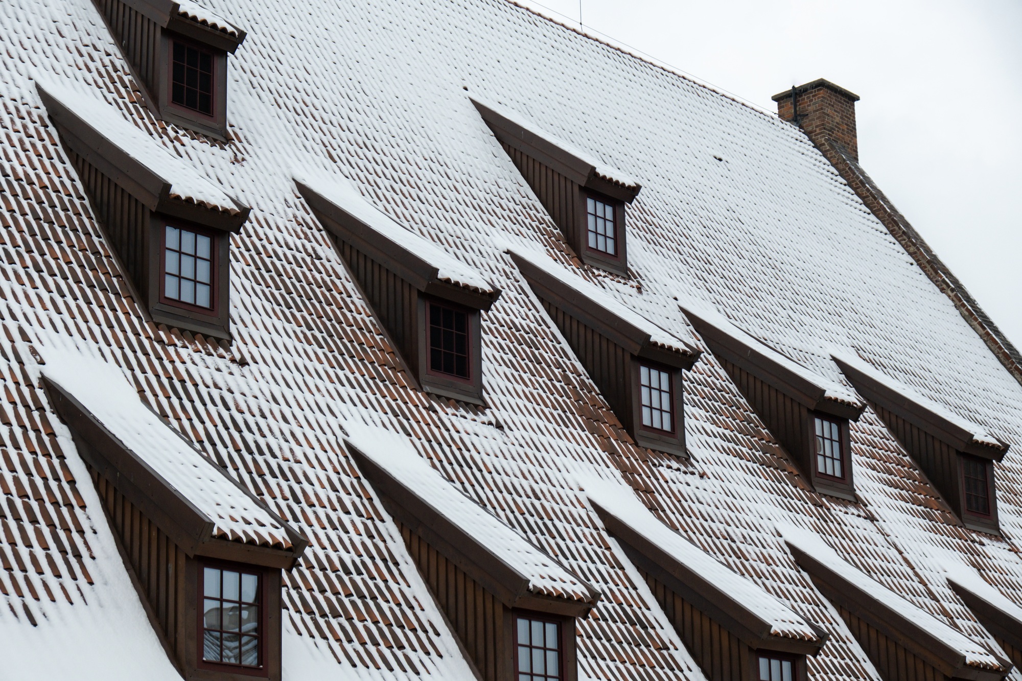 Snow falling on the roofs of the city. Snow-covered brown metal tiles roof of European house with